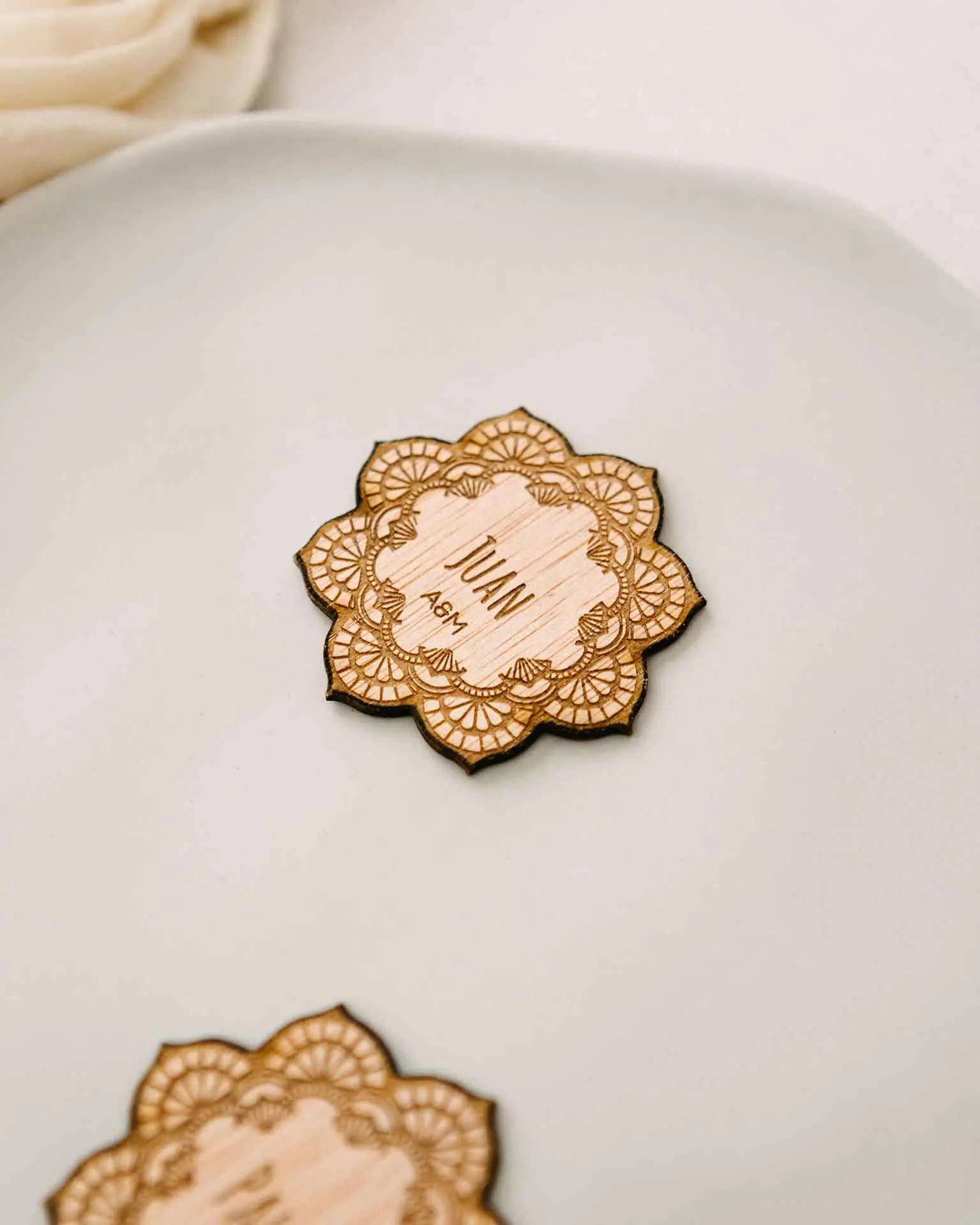 Marcasitio de madera con forma de mandala y nombre del invitado grabado en el centro, colocado sobre un plato