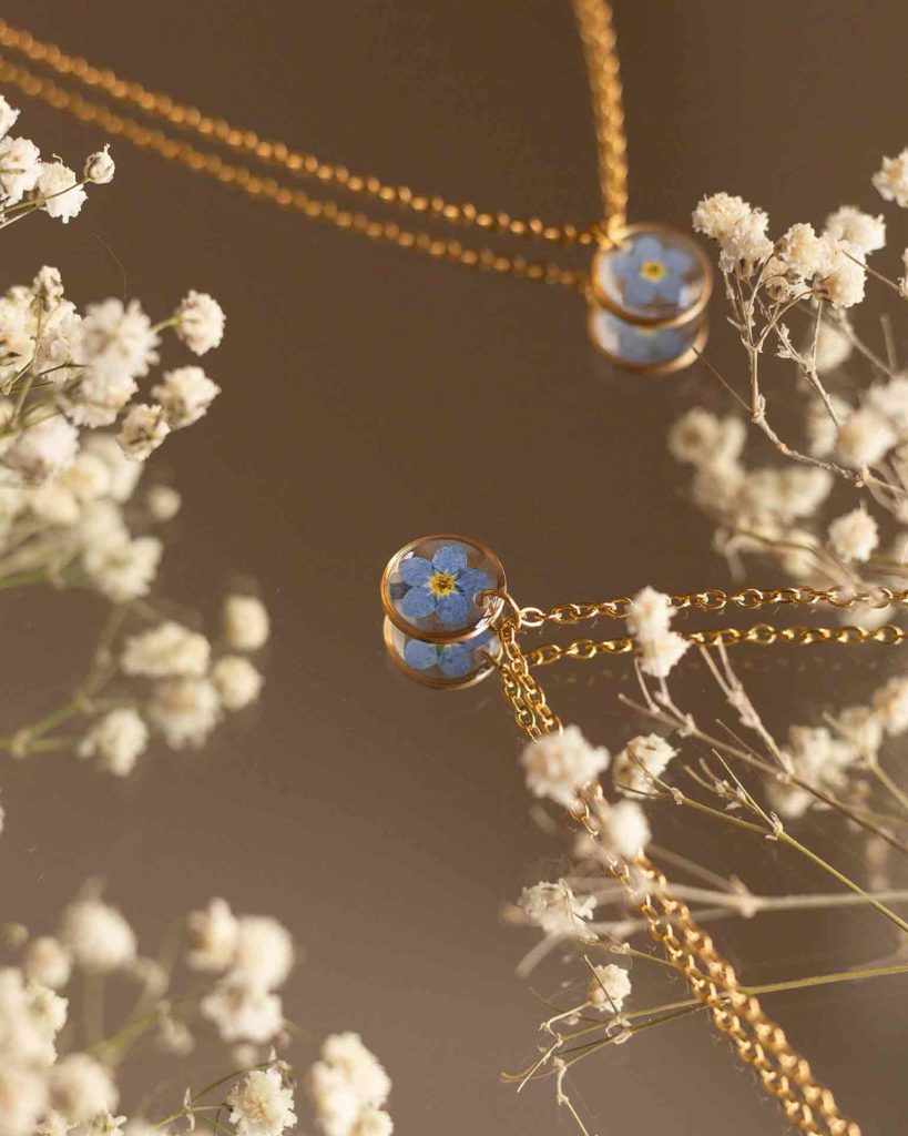 Primer plano del colgante con flor No me olvides en dorado