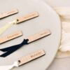 Primer plano del grabado con el nombre del invitado sobre madera, con lazo decorativo en color