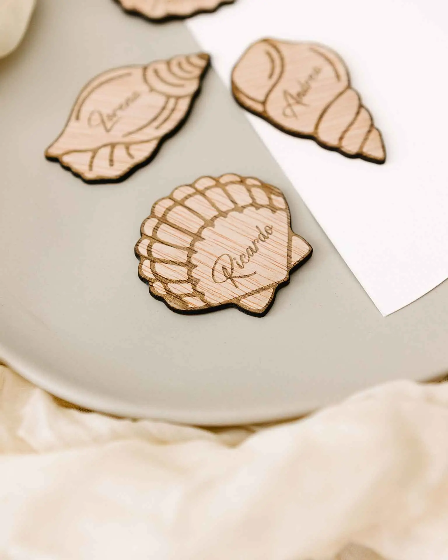 Marcasitio con diseño de concha abierta, grabado sobre madera con el nombre del invitado
