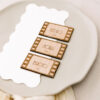 Marcasitios de madera con forma de fotograma de pelu00edcula grabado con el nombre del invitado, colocado sobre un plato