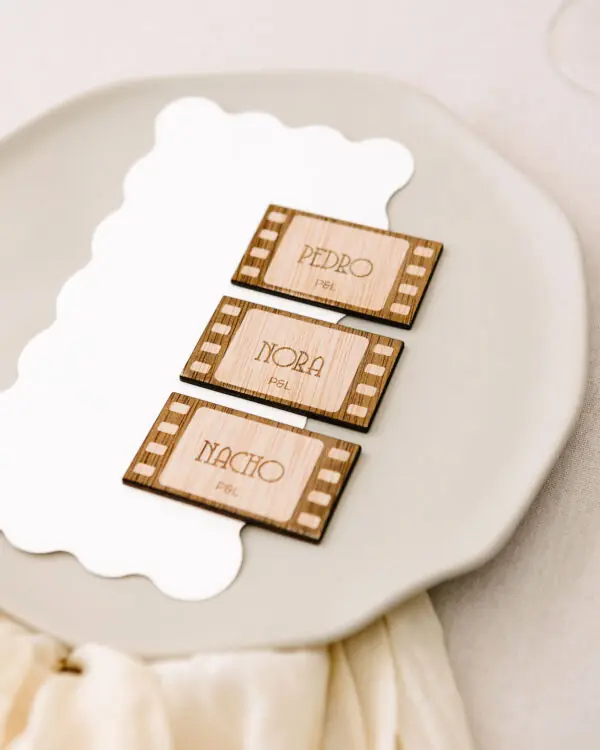 Marcasitios de madera con forma de fotograma de película grabado con el nombre del invitado, colocado sobre un plato