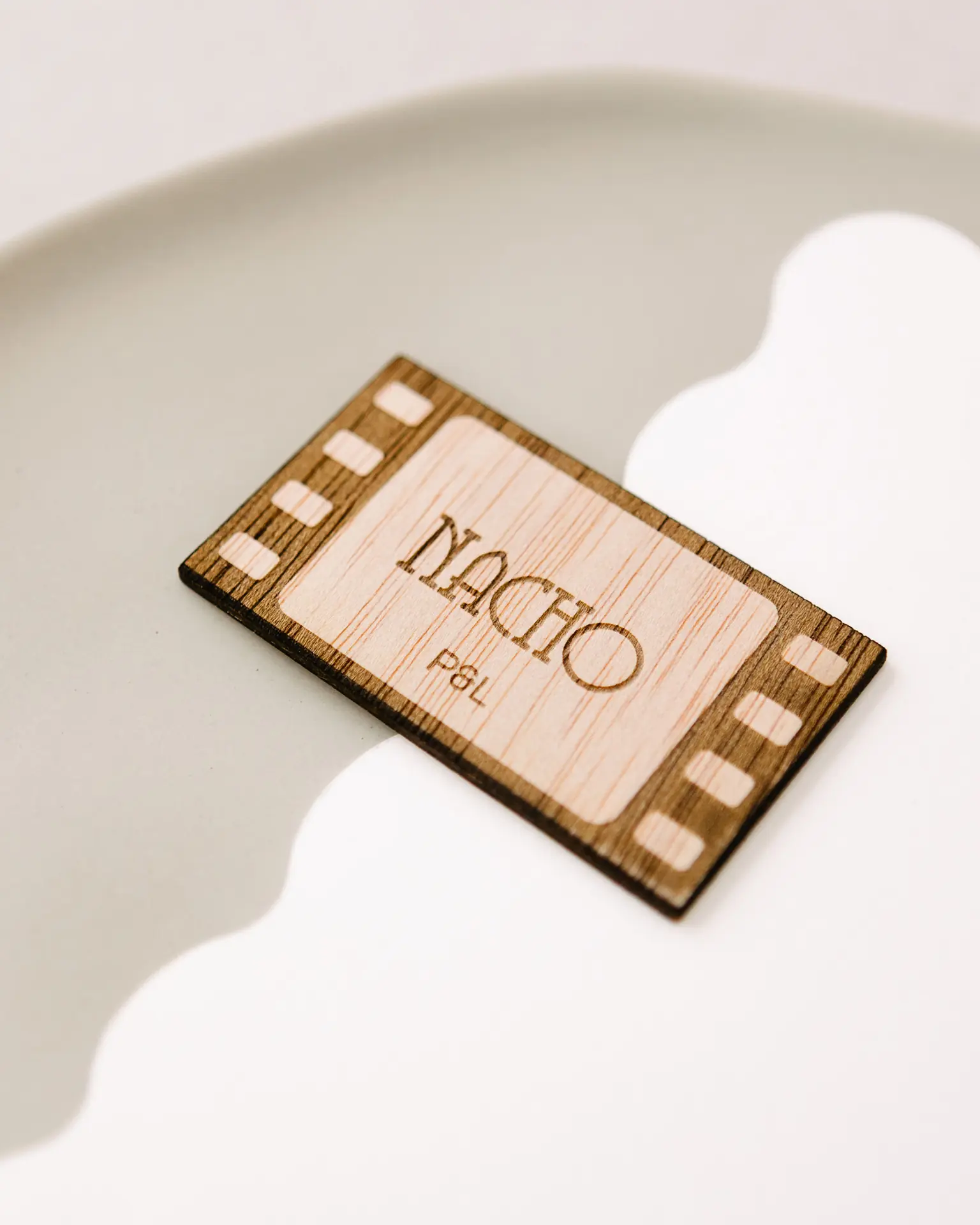 Primer plano del grabado con el nombre del invitado en el marcasitio de madera con forma de fotograma