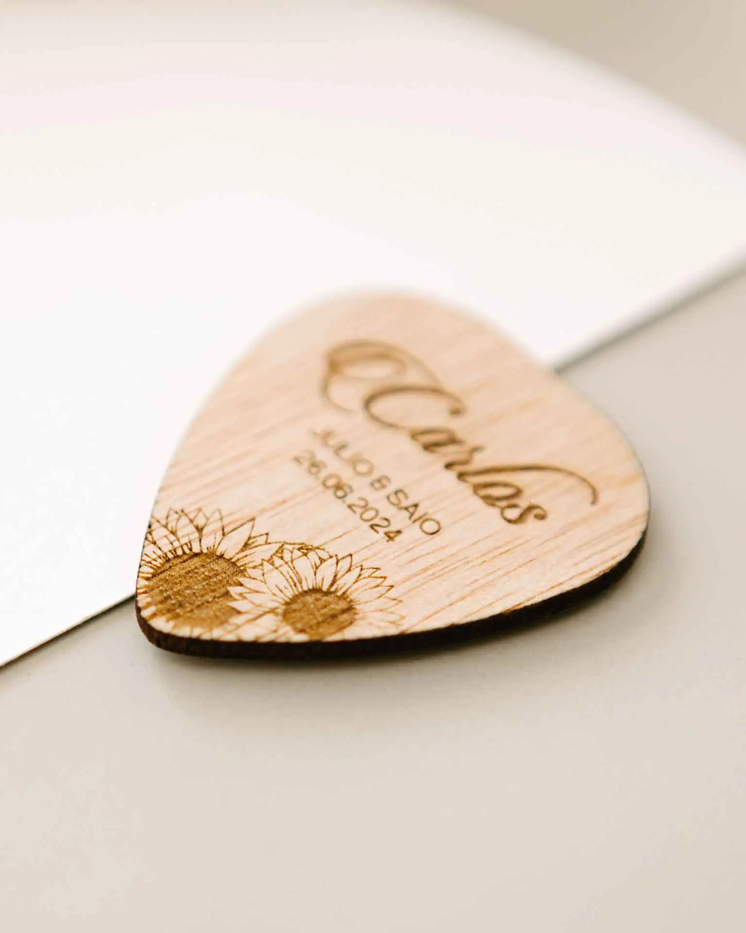 Marcasitio de madera con forma de púa, tipografía caligráfica y detalles grabados de girasoles