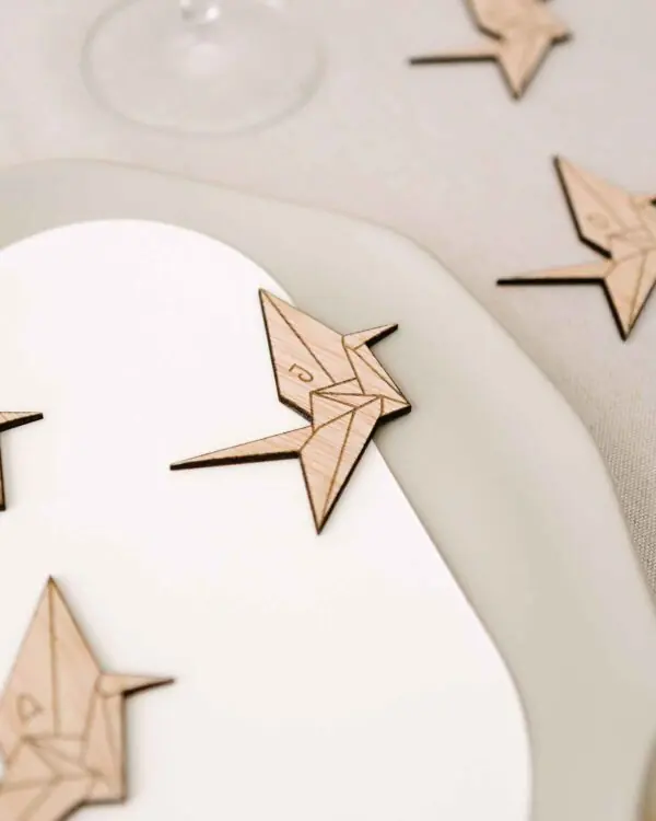 Marcasitio de madera con forma de grulla de papel origami y la inicial del invitado, colocado sobre un plato