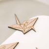 Primer plano del grabado con la inicial sobre la forma de grulla de origami en madera