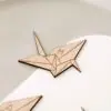 Primer plano del grabado con la inicial sobre la forma de grulla de origami en madera