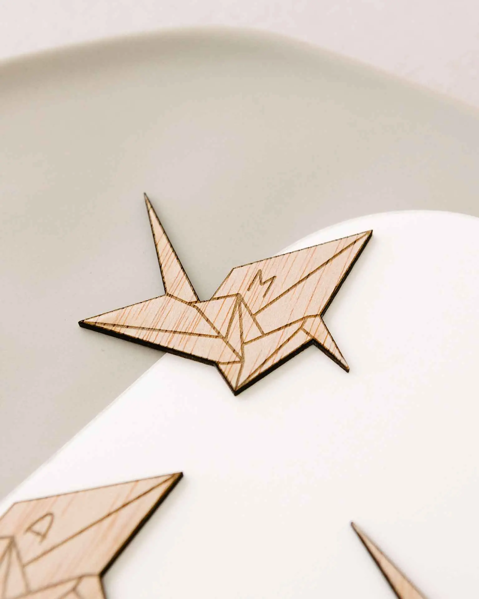 Primer plano del grabado con la inicial sobre la forma de grulla de origami en madera
