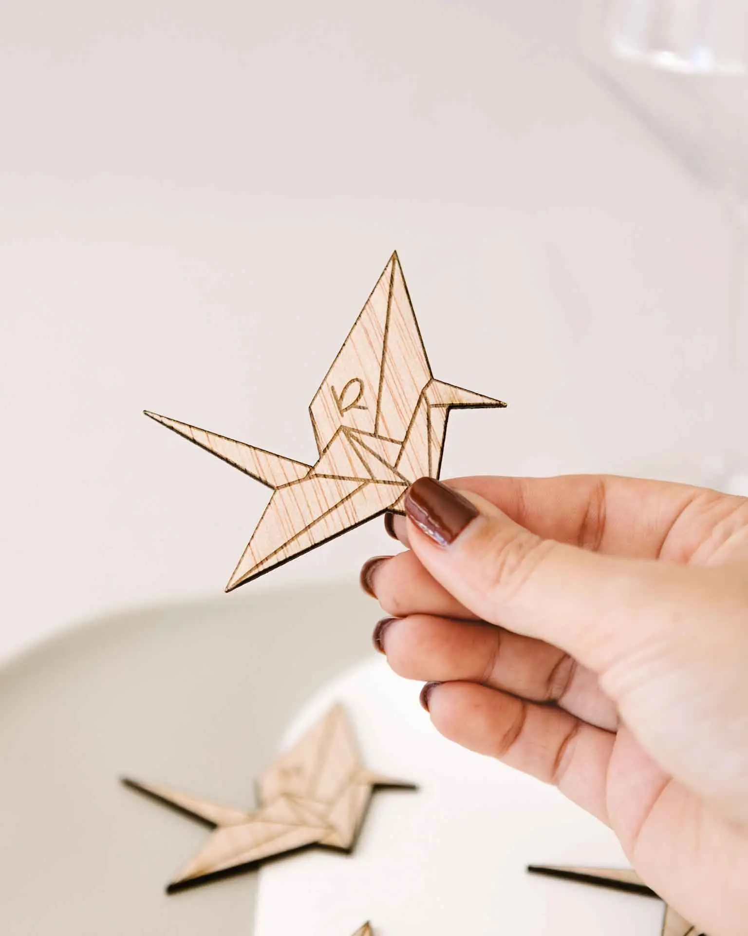 Tamaño real del marcasitio Grulla Origami mostrado en la mano, con grabado personalizado en madera