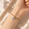 Pulsera No me olvides dorada en la muu00f1eca con charm de flor azul y detalle imantado.